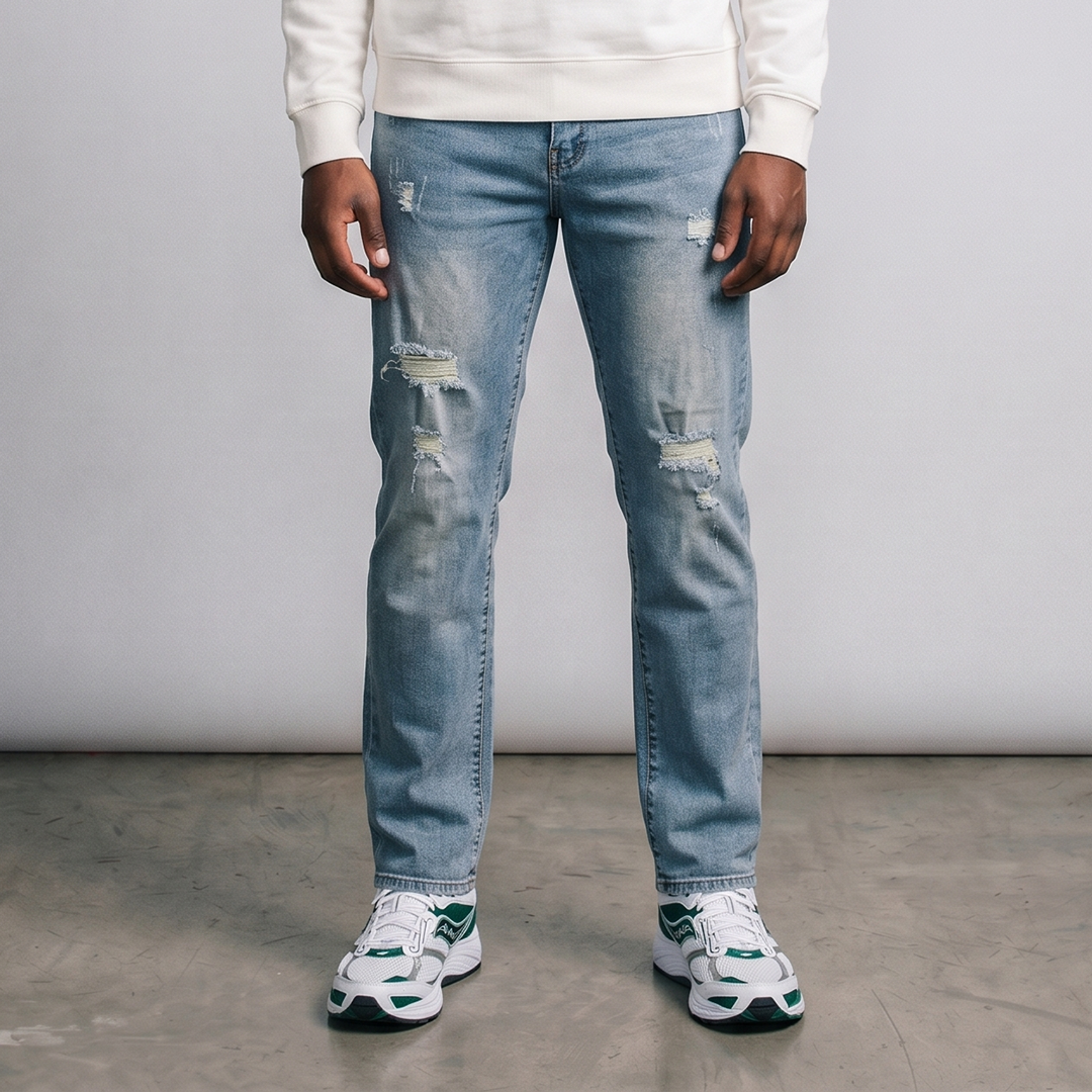Person wearing distressed blue jeans and white sneakers on a plain background