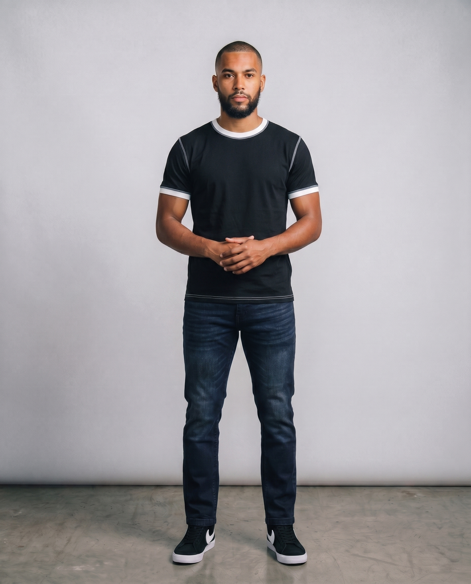 Man wearing a black t-shirt with white trim and dark jeans against a plain background